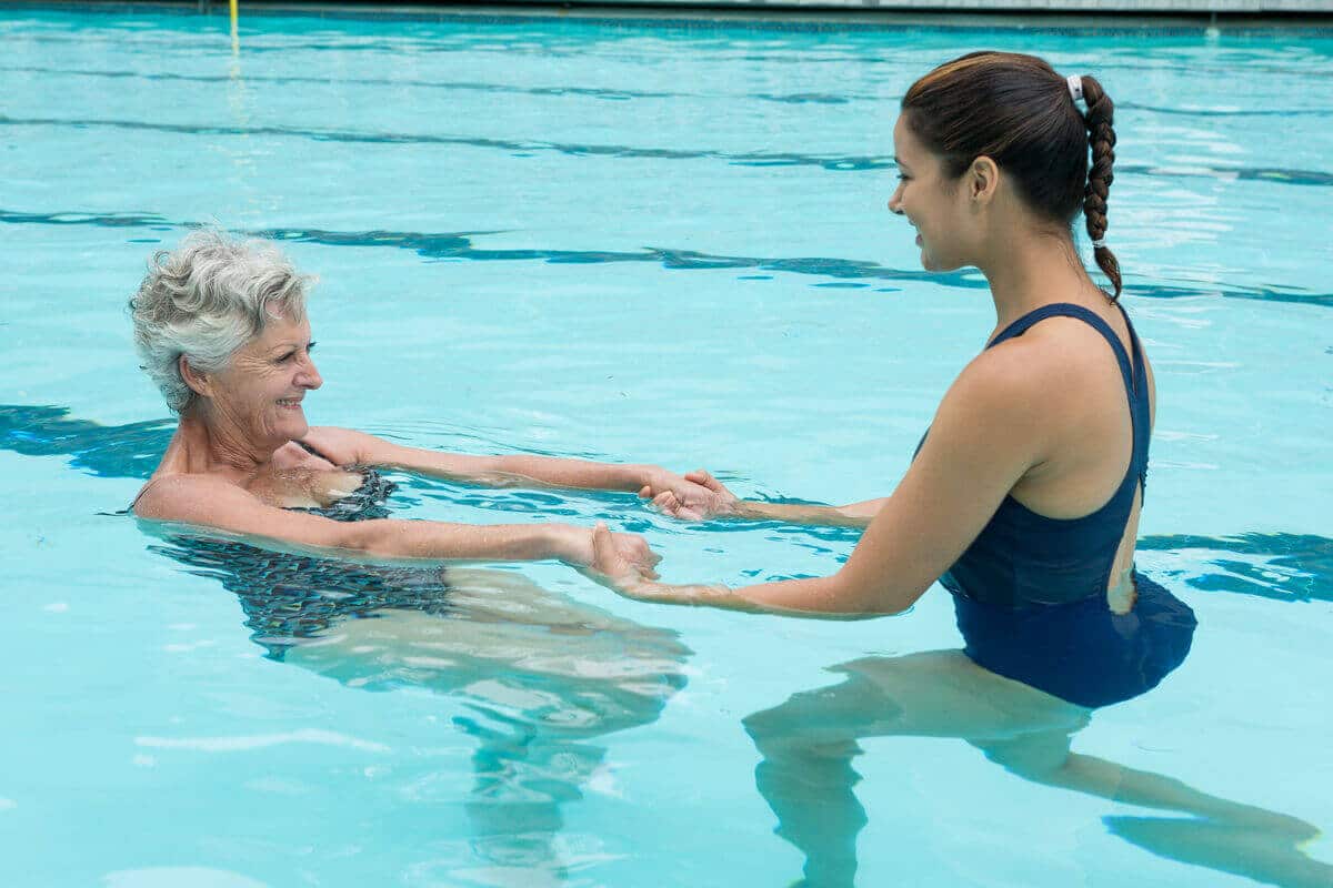Terapia ocupacional medio acuático, mujer mayor entrenando con pesas en la piscina